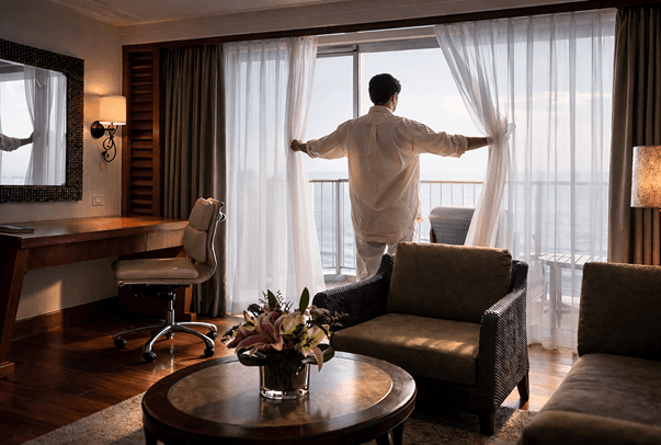 Guest opening curtains to a balcony view in a luxury hotel suite