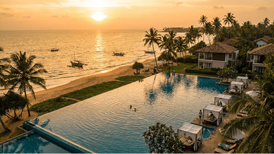 Aerial sunset view of a luxury resort pool beside a tropical beach